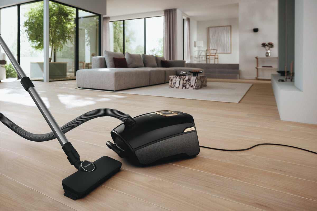 Miele Guard L1 AllFloor canister vacuum on a wood floor with a couch in the background