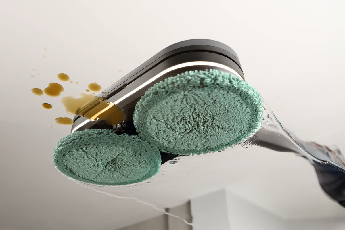 Underside of the Miele Triflex AquaTwister with two AquaPads fitted, wiping a spill from a hard floor.