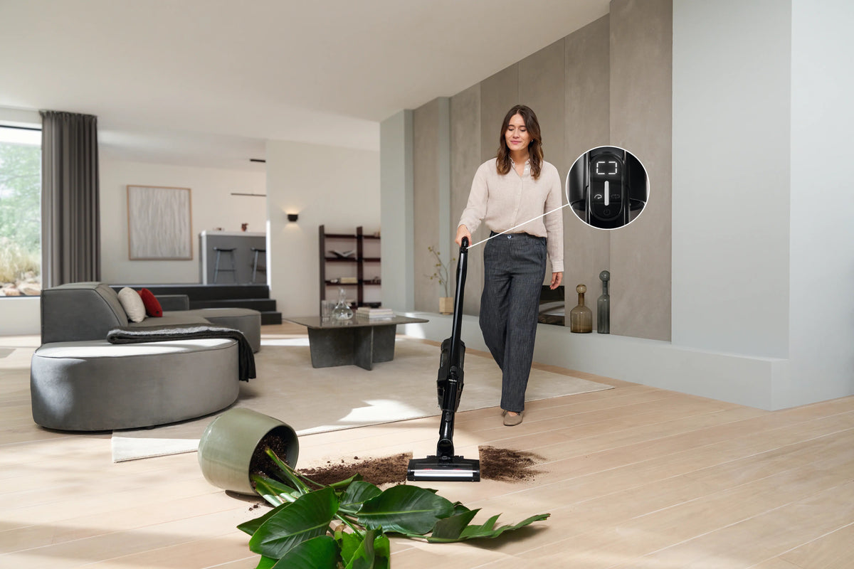 Miele Triflex HX3 Aqua vacuuming spilled potting soil from a wood floor, with a close-up of its handle controls.