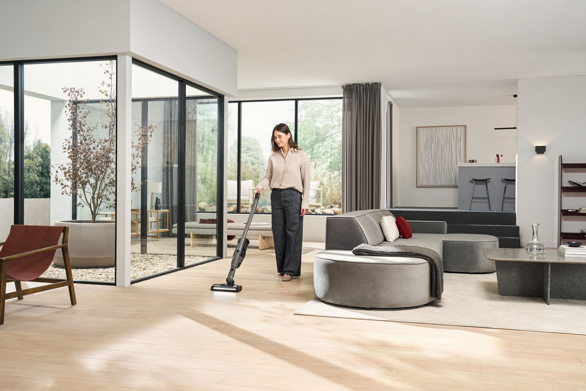 Woman vacuuming a hard floor in a bright living room with the Miele Triflex HX3 Hardfloor in Casa Grey.