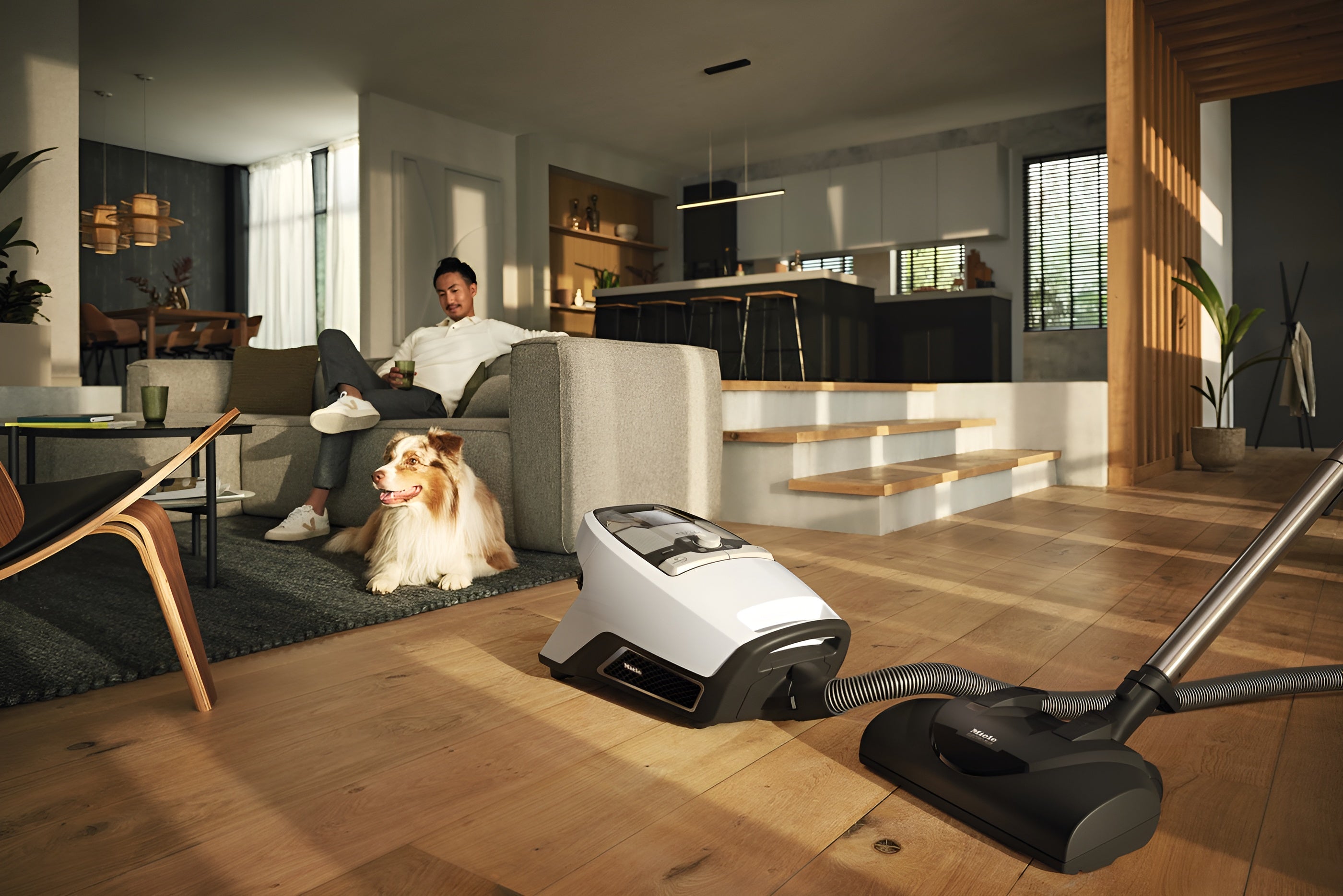 Person sitting on a couch with a dog in a modern living room, using a Miele Blizzard CX1 Cat & Dog Bagless Vacuum cleaner.