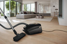 Miele Guard L1 AllFloor canister vacuum on a wood floor with a couch in the background