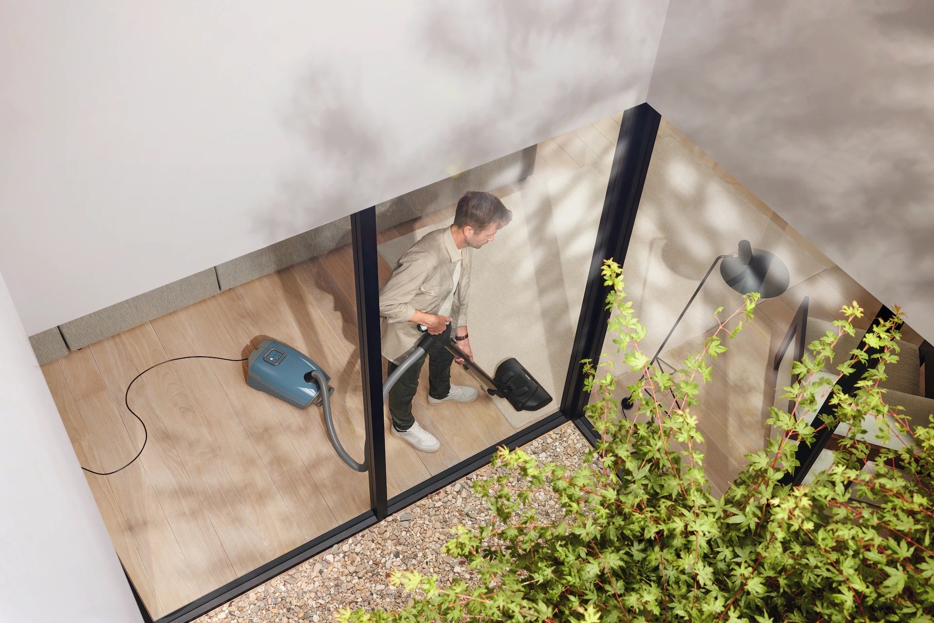 Person using a Miele Guard L1 Nordic Blue vacuum cleaner on a patio with a glass wall