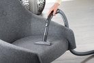 Person cleaning a gray chair with a Miele canister vacuum cleaner.