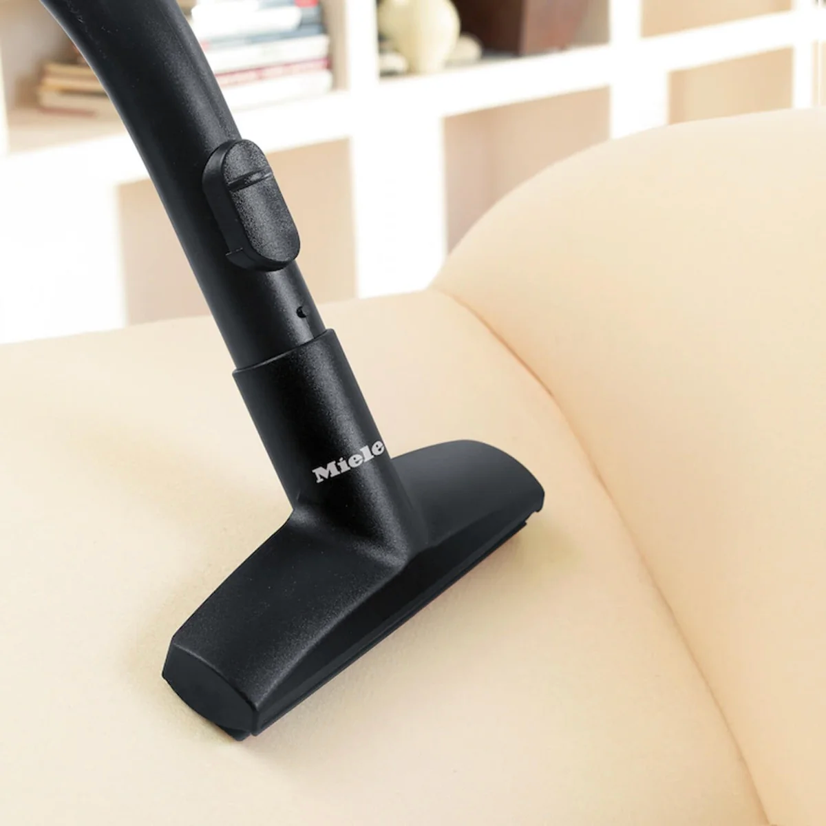 Black Miele vacuum cleaner attachment on a beige sofa