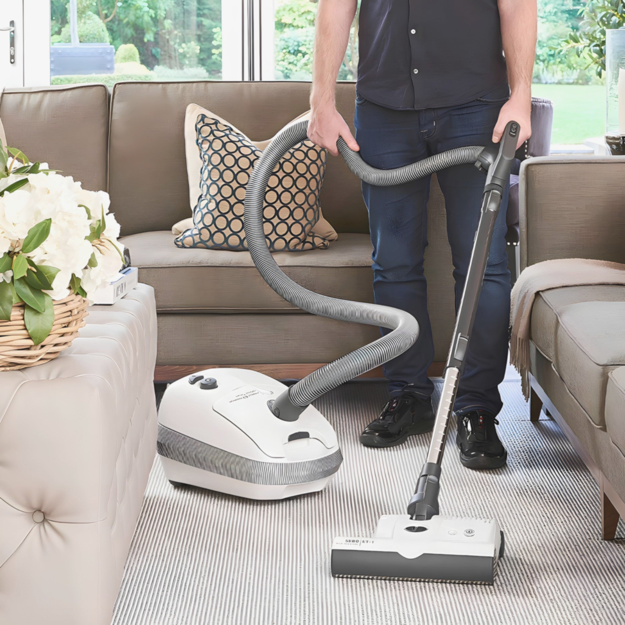 Man vacuuming a living room rug with a white SEBO AIRBELT E3 Premium canister vacuum and its ET-1 powerhead