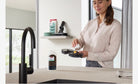 Adding Miele FloorClean concentrate to the water tank of a Miele AquaTwister wet-cleaning attachment in a kitchen.