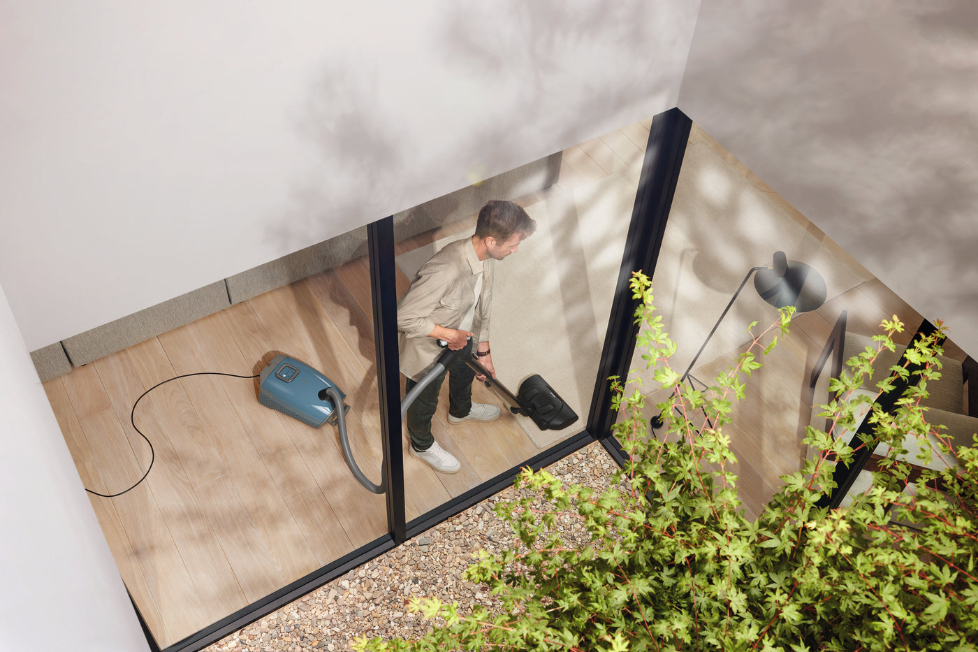 Person using a Miele Guard L1 in Nordic Blue by a glass wall.