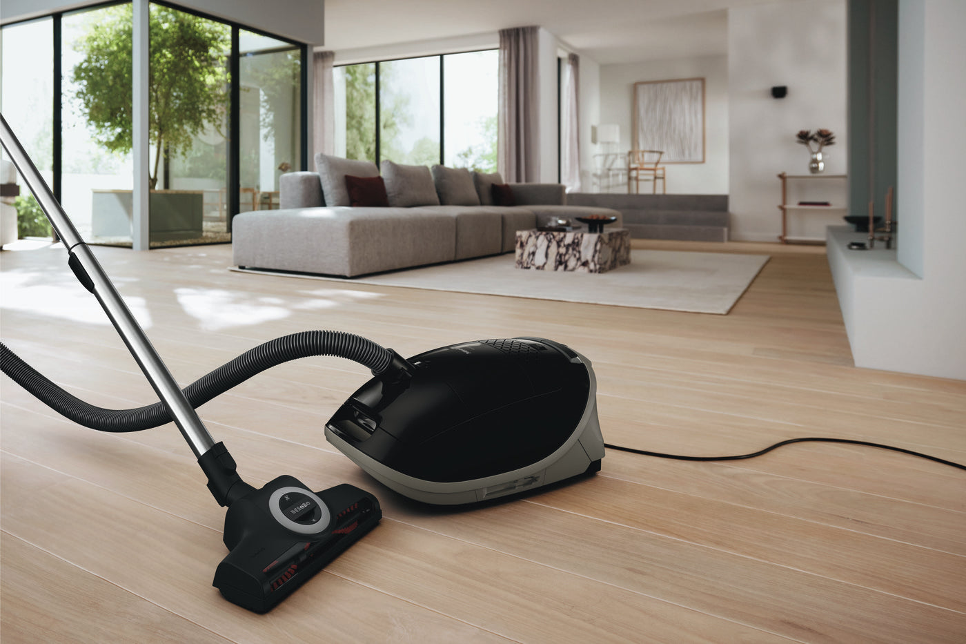 Black Miele Guard M1 Cat & Dog canister vacuum in a modern living room with wood floors.