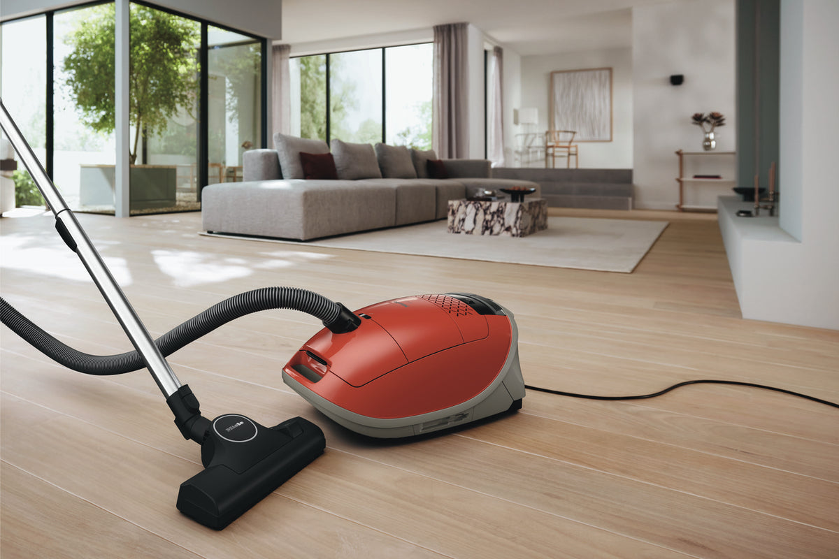 Red Miele Guard M1 Terra Red canister vacuum in a modern living room with wood floors.