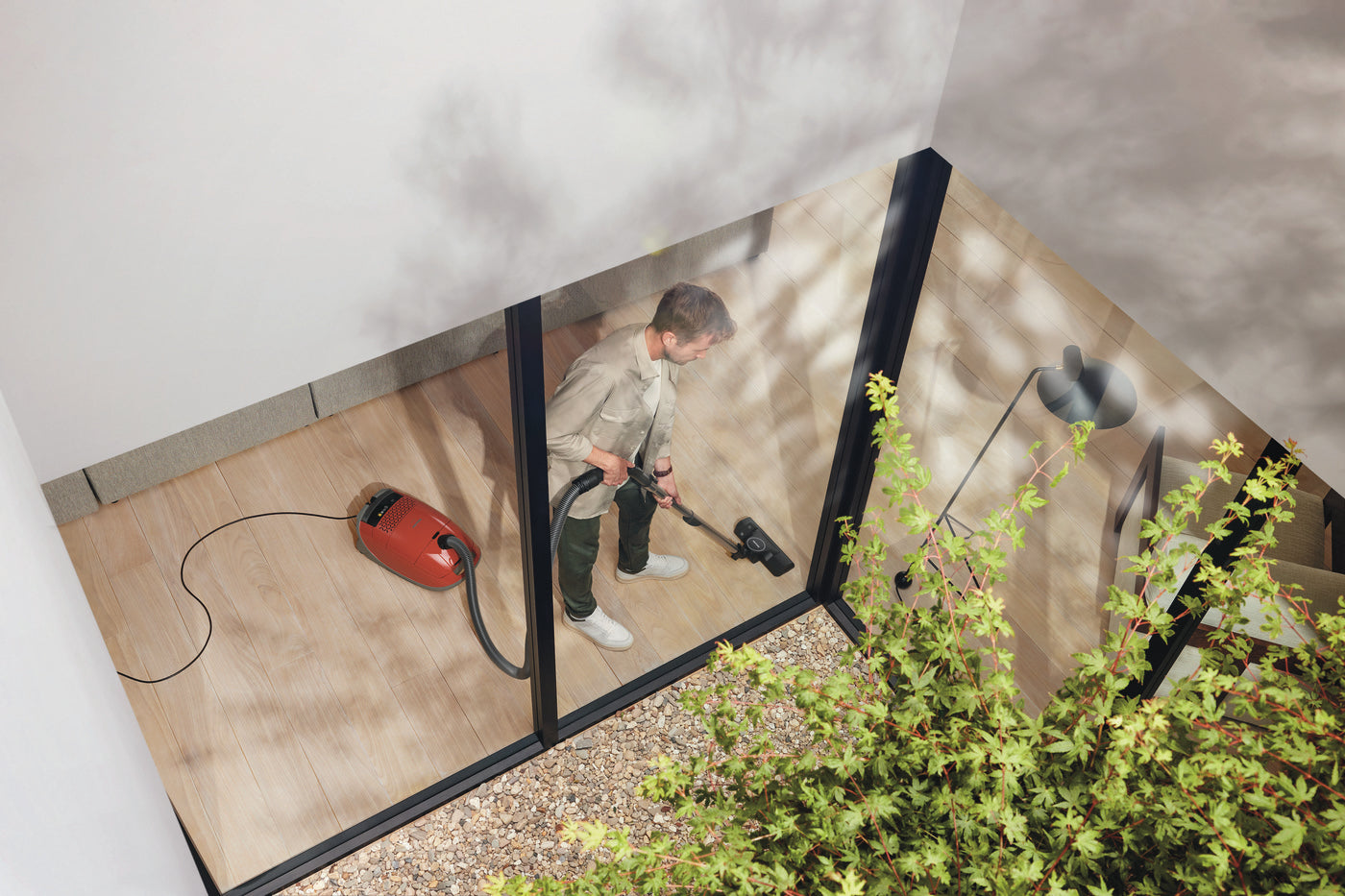 Person walking with the red Miele Guard M1 Terra Red canister vacuum on an outdoor patio.