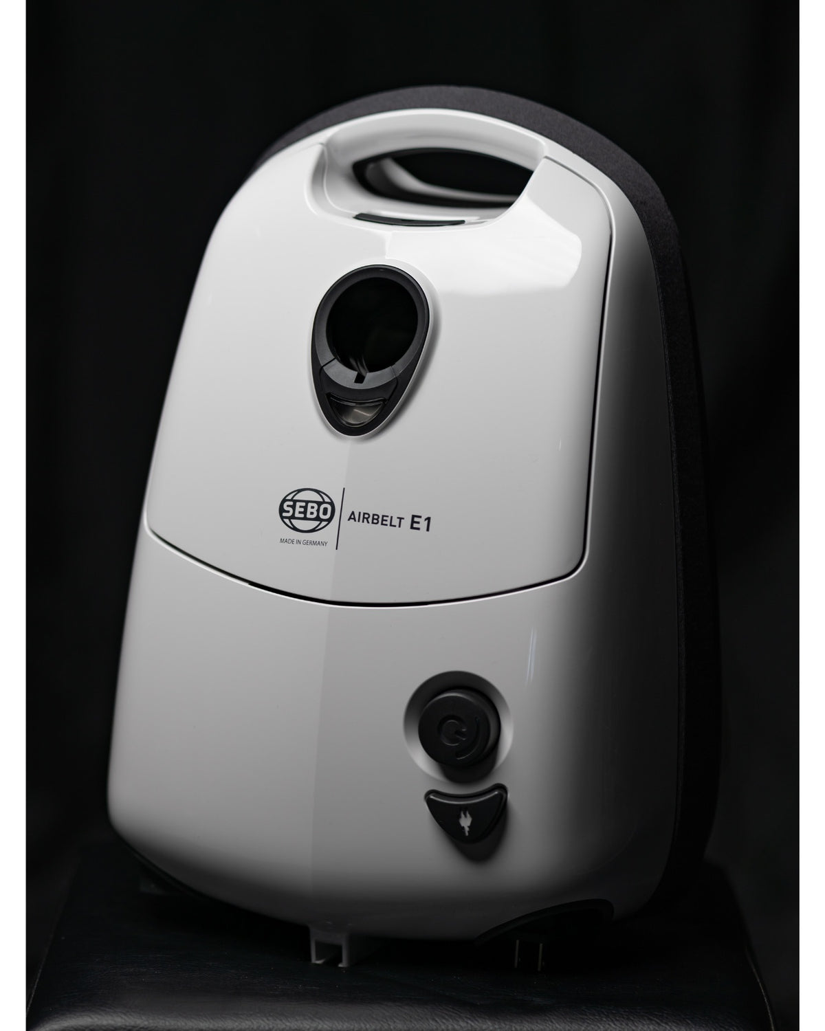 Close-up of the white SEBO Airbelt E1 Kombi canister vacuum's front panel and logo.
