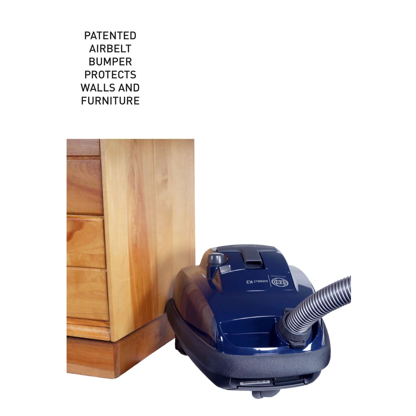 Dark blue SEBO Airbelt K2 Kombi canister vacuum next to a wood furniture corner, showing the patented Airbelt bumper that protects walls and furniture.